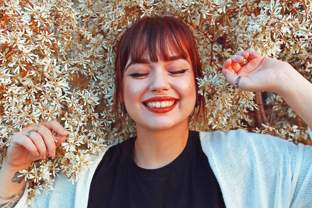 Une femme rousse couchée sur un lit de fleurs elle ales yeux fermé, elle sourit on peux penser qu'elle a un orgasme